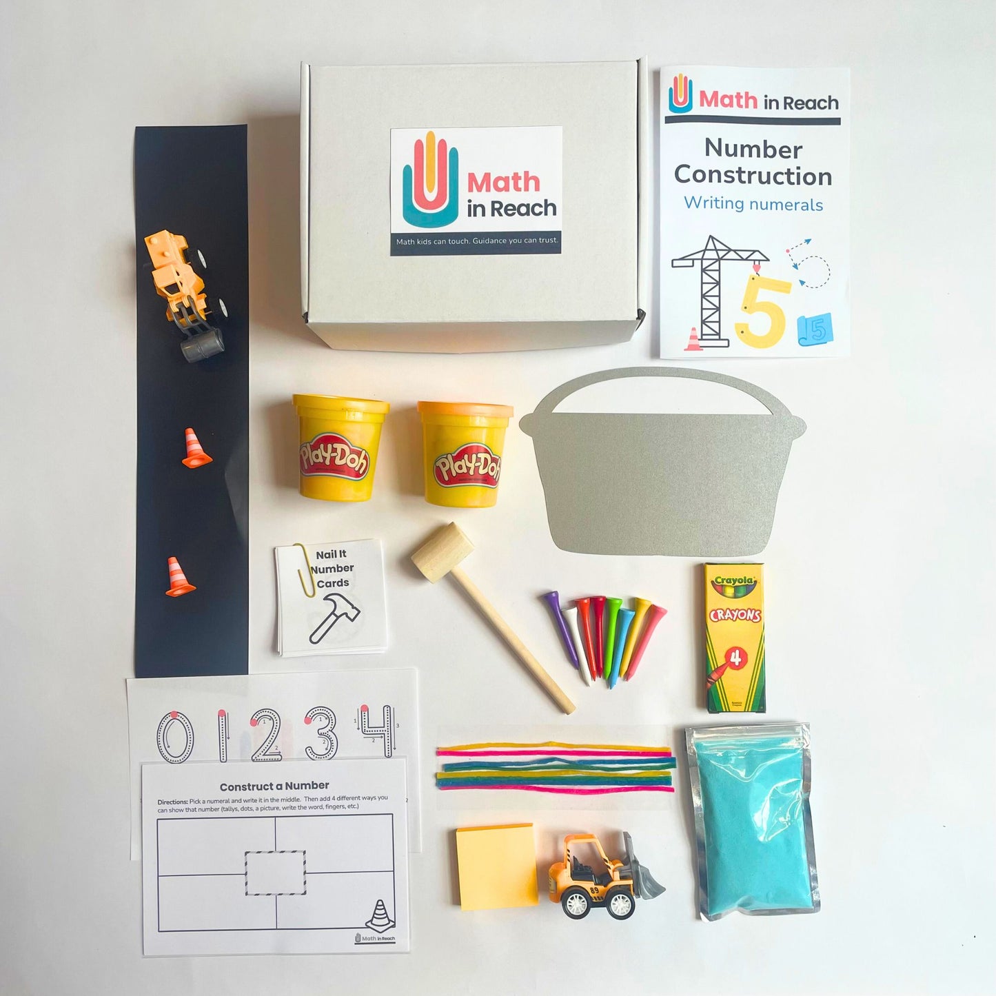 Construction-themed Math in Reach monthly kit for kids ages 4–6. Includes Play-Doh, toy trucks, number cards, craft sticks, hammer, and paper practice to support writing numerals.